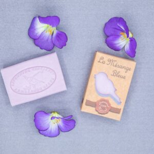 Savons à la violette posés sur un fond bleu avec des fleurs violettes en décoration