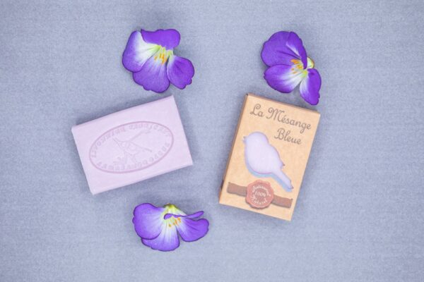 Savons à la violette posés sur un fond bleu avec des fleurs violettes en décoration