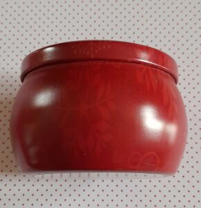 Vue de côté d'une boite ronde vintage contenant une bougie parfumée, la couleur est rouge et elle est décorée de divers flocons de neige de couleur rouge plus clair que la boîte et de diverses tailles