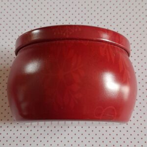 Vue de côté d'une boite ronde vintage contenant une bougie parfumée, la couleur est rouge et elle est décorée de divers flocons de neige de couleur rouge plus clair que la boîte et de diverses tailles