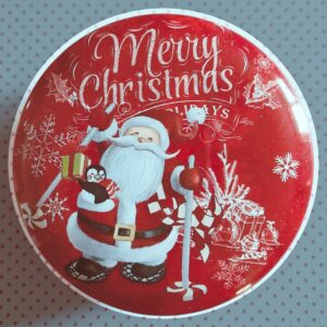 Bougie parfumée dans une boîte ronde rouge vintage avec en décor une illustration d'un père noël, de flocons de neiges, de cadeaux et d'une inscription "merry christmas"