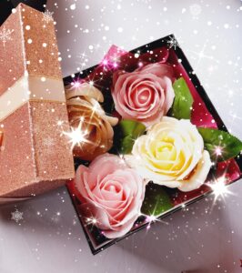 Boîte de couleur noire avec le couvercle rose gold pailleté et un ruban autour, contenant 4 savons en forme de roses, 2 de couleur rose, 1 de couleur blanc et 1 de couleur beige