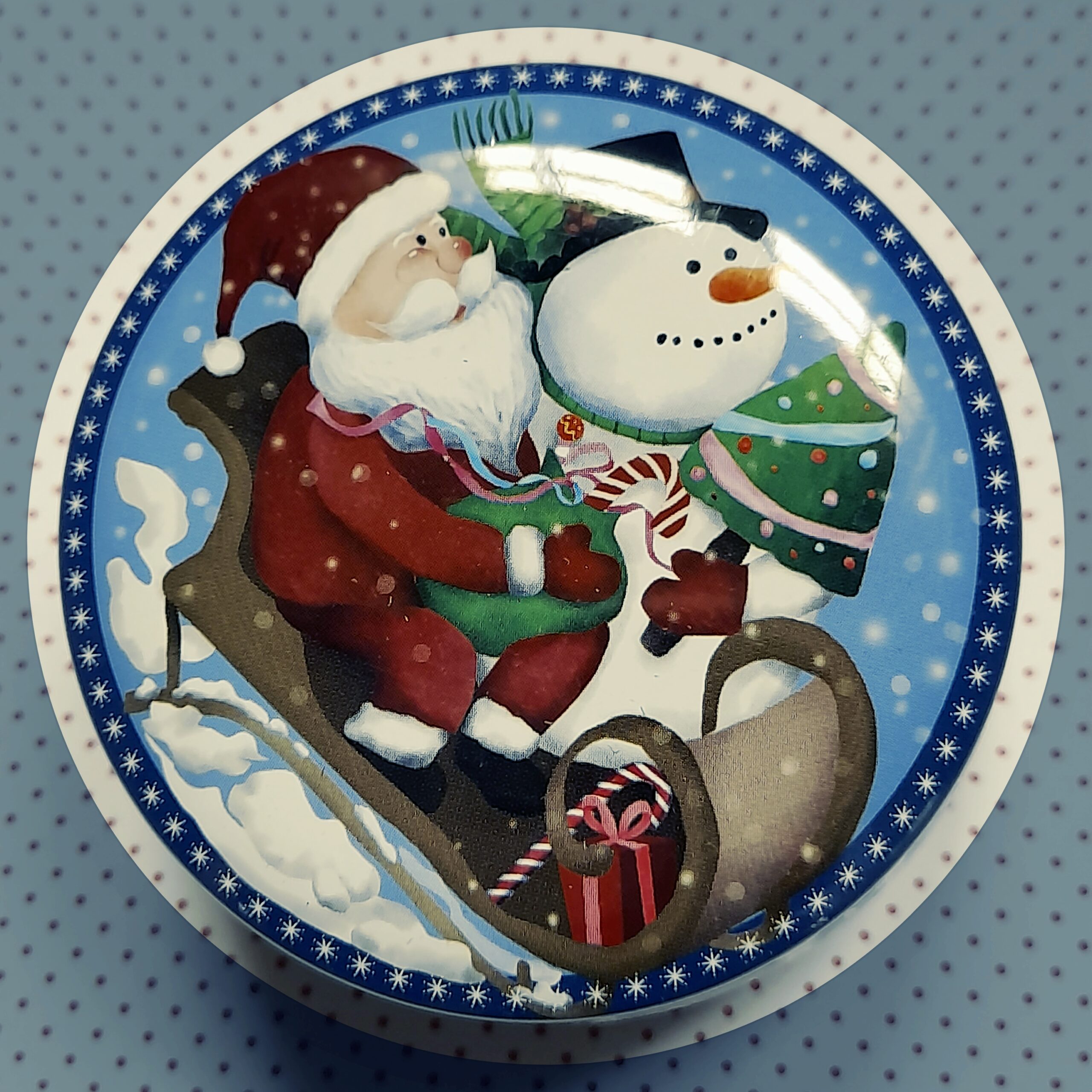 Bougie parfumée dans une boîte ronde vintage avec en décor un père noël, un bonhomme de neige et un sapin sur un traineau