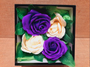 Vue intérieur d'un coffret cadeau avec 4 roses en savons, 2 de couleur violet et 2 de couleur crème