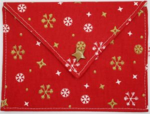 Pochette à savon Solange, rouge avec des flocons de neiges et des étoiles de différentes tailles de couleurs or et blanc et un bouton pression en forme d'étoile de couleur or
