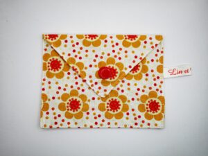 Pochette à savon blanche avec des motifs floraux psychédélique années 70 de couleurs orange et jaune clair, avec un bouton pression rond rouge