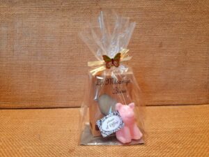 Sachet cadeau contenant un savon parfumé et un savon en forme de cochon de couleur rose, sur un fond en jute