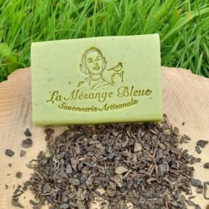 Savon artisanal naturel parfumé au thé vert posé sur un rondin de bois sur de l'herbe avec du thé vert en vrac.
