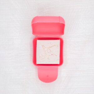 Boîte à savon petit modèle de couleur rose avec un savon invité blanc dedans, sur un fond gris clair