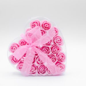 Coffret en forme de cœur contenant 24 savons en forme de roses roses, entouré d'un ruban rose à pois blanc, sur un fond blanc