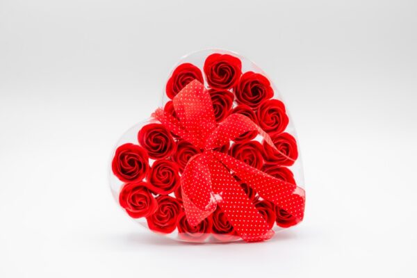 Coffret en forme de cœur contenant 24 savons en forme de roses rouges, entouré d'un ruban rouge à pois blanc, sur un fond blanc