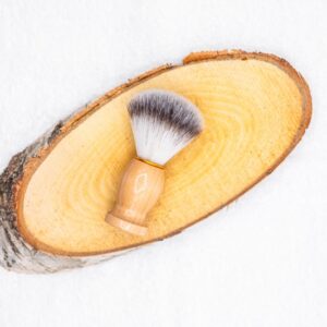 Blaireau à barbe avec un manche en bois posé sur un rondin en bois, sur un fond blanc