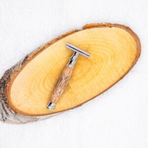 Rasoir à barbe avec un manche en bois posé sur un rondin en bois, sur un fond blanc