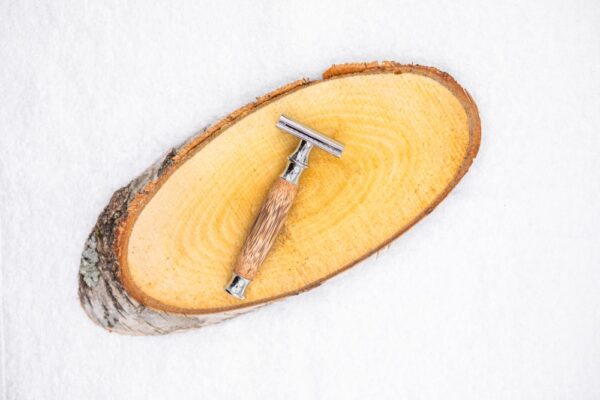 Rasoir à barbe avec un manche en bois posé sur un rondin en bois, sur un fond blanc