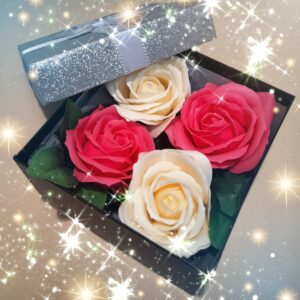 Boîte cadeau noire avec le couvercle gris pailleté et un ruban argenté autour, contenant 4 savons en forme de roses, 2 de couleur blanche et 2 de couleur rose