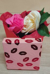 Boîte de couleur rose et rouge décorée de bisous, contenant une un savon en forme de rose de couleur rose et un savon en forme de rose de couleur blanche