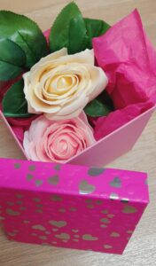Vu intérieure d'une boîte rose décorée de cœurs, contenant une un savon en forme de rose de couleur rose et un savon en forme de rose de couleur blanche