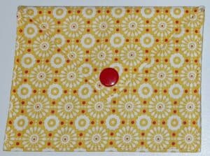 Pochette à savon Louisette, couleur jaune avec des fleurs rondes de couleurs blanches et des points rouges. Bouton pression rond de couleur rouge.