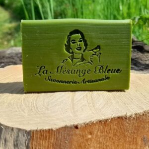 Savon artisanal naturel à la spiruline BIO, posé sur une tranche de bois dans un décor naturel de verdure coordonné à la couleur verte du savon.